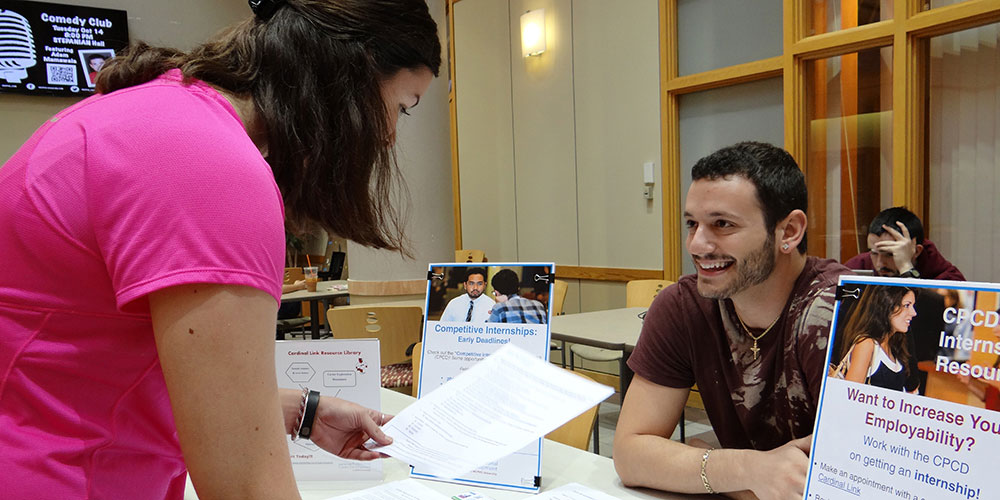 man sitting at desk smiling and woman holding paper